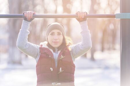 Attractive girl involved in sports workout on a horizontal bar on a sunny winter day. The concept of...