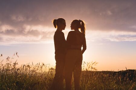 Silhouette portrait of a romantic young hipster couple in profile. Standing in an embrace on nature in the tall grass The concept of a young family and a happy future togetherの写真素材