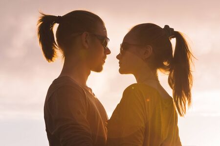 Silhouette portrait of a romantic young hipster couple in profile. Standing in an embrace on nature. The concept of a young family and a happy future togetherの写真素材