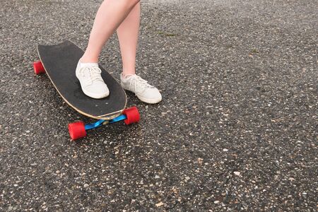 Close-up of female legs in rag sneakers on a longboard on the background of asphalt at sunset. Big...