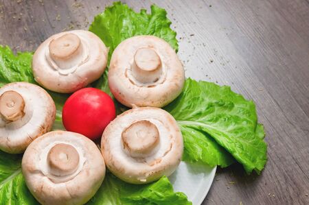 Closeup of white mushrooms with green salad leaves with tomato on a dark wooden table. Vegetarian healthy foodの写真素材