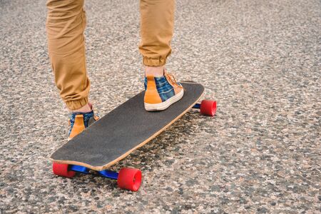 Close-up of male legs in rag sneakers on a longboard on the background of asphalt at sunset. Big skateboard with man legs. Youth leisure conceptの写真素材