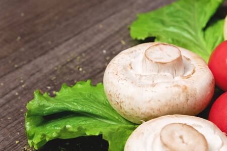 Closeup of white mushrooms with green salad leaves with tomato on a dark wooden table. Vegetarian healthy foodの写真素材