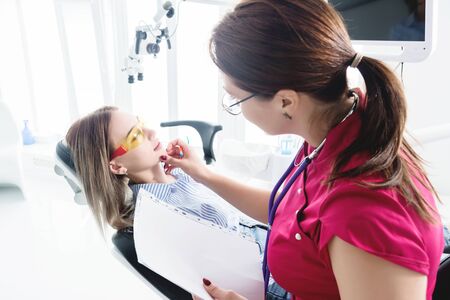 Dentist woman doctor talking to a young patient sitting on the dentist chair in a medical office. The first conversation with the client and external visual inspectionの写真素材