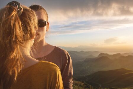 Conceptual portrait of a young couple on the background of a sunset sky and a beautiful mountain valley. Half of the face of a young guy in sunglasses and a girl standing backの写真素材