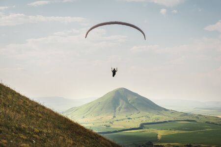 A paraglider flies in the sky in a cocoon suit on a paraglider above the mountain on a sunny summer...