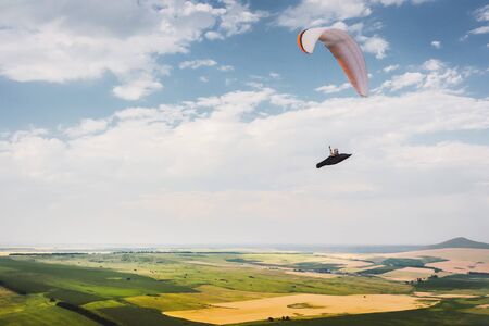 A paraglider flies in the sky in a cocoon suit on a paraglider over the Caucasian countryside with hills and mountains. Paragliding Sport Conceptの写真素材