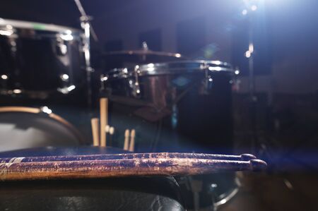 Close-up of used drumsticks lie on a drummers chair against the background of a drum kit and flare...