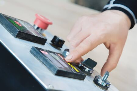 Close-up of a male hand on a dashboard controlling production equipment with buttons and displays in a locksmiths workshop for furniture productionの写真素材