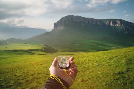 Male hand with a magnetic compass ea against the backdrop of a beautiful landscape at sunset. The concept of navigating the search for your own path and orientation to the cardinal pointsの写真素材