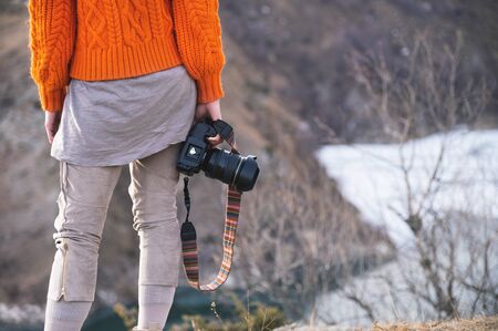 A female hand holds a camera against a mountain landscapeの写真素材