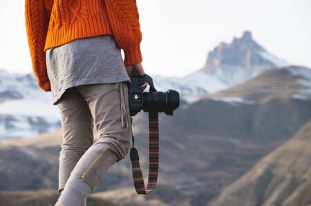 A female hand holds a camera against a mountain landscape