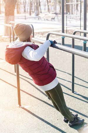 Portrait of a sports girl doing workout in the winter on an outdoor sports field. Exercises on...