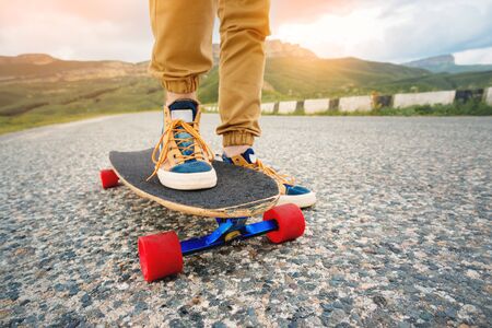 Close-up of male legs in rag sneakers on a longboard on the background of asphalt at sunset. Big skateboard with man legs. Youth leisure conceptの写真素材