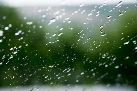 Natural background Drops on both sides of the glass from the rain and from the fogging abstract view, raindrops against the blue glass and the blurred landscape of the gradient of blue and green.の写真素材