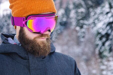 Close-up portrait of an attractive young bearded man in a knitted winter hat and ski mask with...