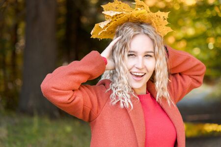 Portrait of attractive caucasian young blonde girl in red coat with a bouquet of fallen yellow leaves smiling in the autumn forest. The concept of autumn and fall holidays and weekendsの写真素材