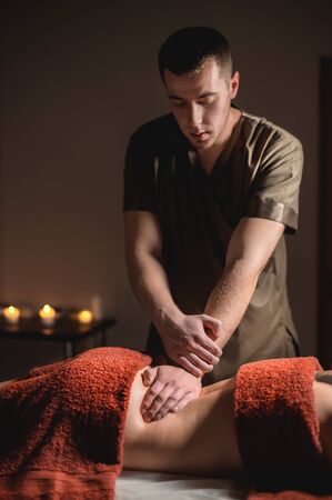 Close-up of the hands of a male masseur doing back massage to a girl at the spa. Low key high contrast shallow depth of fieldの写真素材