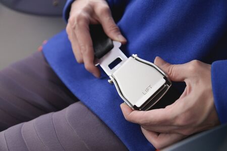 Close-up of a young woman fastens a seat belt while sitting in a passenger airplane chair by the...
