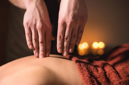 Close-up of the hands of a male masseur doing back finger massage to a girl at the spa. Low key high contrast shallow depth of fieldの写真素材