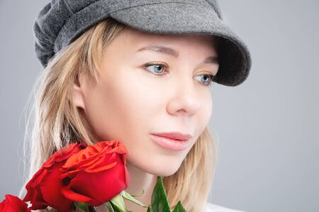 Close-up portrait of an attractive caucasian blonde girl in a retro cap with roses in her hands and looking to the sideの写真素材