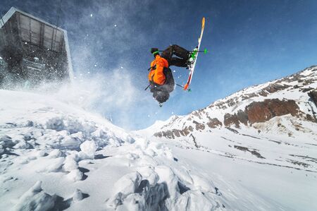 Low angle view athlete skier in an orange jacket does a back flip with flying powder of snow against...