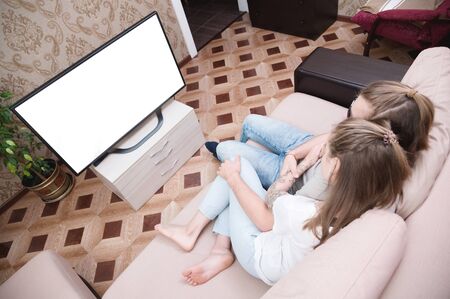 Attractive young long-haired couple hugging on a sofa at home in isolation watching tv. The concept of spending time with loved ones during a pandemic.の写真素材