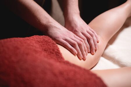 Close-up low key on woman's thigh massage in a professional premium spa salon, man masseur does in a dark massage roomの写真素材