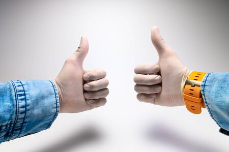 A two male hand in a rubber medical glove and a blue denim shirt with a yellow strap shows a thumb...