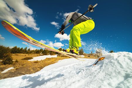 Girl skier in flight after jumping from a kicker in the spring against the backdrop of mountains and blue sky. Close-up wide angle. The concept of closing the ski season and skiing in spring.の写真素材