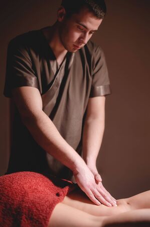 Close-up professional calf muscle massage to a female client by a male physiotherapist in a massage parlor in a dark office against the background of burning candlesの写真素材