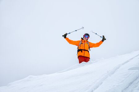 Portrait of a professional skier athlete on a snowy slope in cloudy weather with ski poles raised up