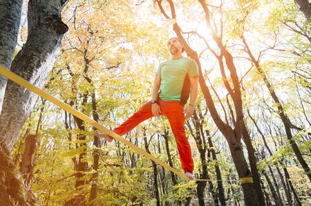 A bearded man aged walks along a slackline in the autumn forest on a sunny afternoon. The concept of...