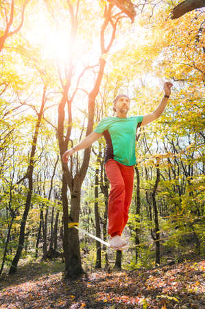 A bearded man aged walks along a slackline in the autumn forest on a sunny afternoon. The concept of...
