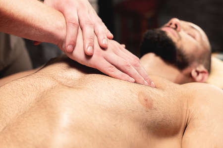 A close-up male masseur does a sports massage of the pectoral muscle to the client athlete in a professional massage salon. The concept of pectoral muscle and breast muscle healthの写真素材