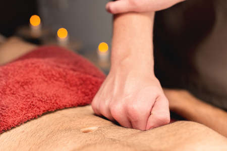 Close-up male masseur massages the stomach of the client while giving a massage of the intestines and abdominal area to a male client athleteの写真素材