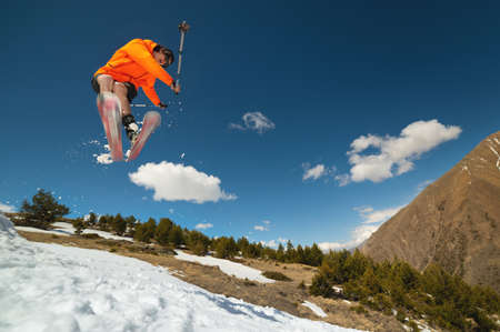 A young stylish man in sunglasses and a cap performs a trick in jumping with a kicker of snow...