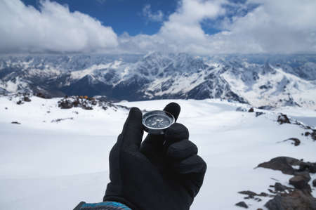 A metal magnetic compass in the hand of a traveler in a black glove against the backdrop of...