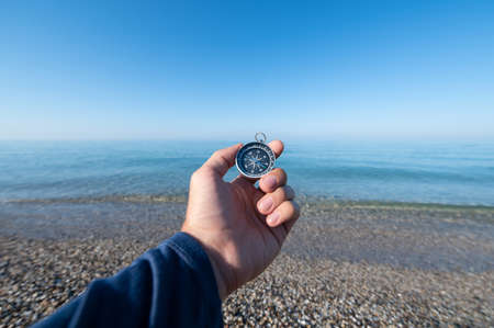 Compass in hand at seacoastA mans hand holds a magnetic compass against the background of a calm...