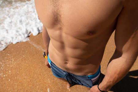Close-up of an athletic physique the body of a young man pectoral muscles press and arms. Top view of a man on the beachの写真素材