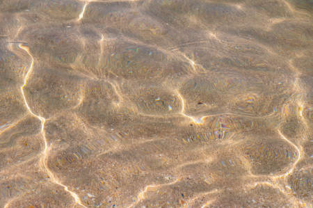 Clear sea water with sun glare and a blurred sandy bottom. Transparent shiny water surface in motion blurの写真素材