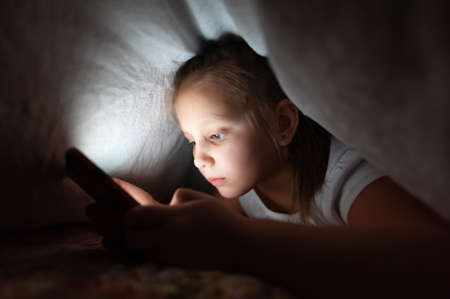 Little girl at night with a smartphone under the covers. Childhood gadget addiction and insomniaの写真素材