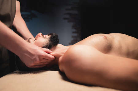 Masseur giving neck massage to young wealthy caucasian athlete in dark room of spa salonの写真素材