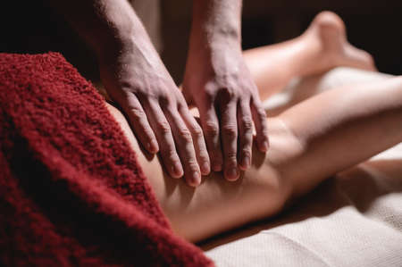Male masseur doing massage of the knee to a woman patient in a dark room of a spa salonの写真素材