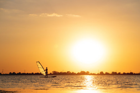 Silhouette woman windsurfer on waves of the bay at beautiful sunsetの写真素材