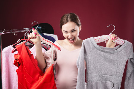 Expressive Caucasian young woman is very surprised shouts looking out of clothes on hangers. Season of low sales prices and price dropsの写真素材