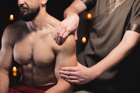 Male athlete has a massage of the shoulder and upper arm muscles in the dark room of the spa massage parlorの写真素材