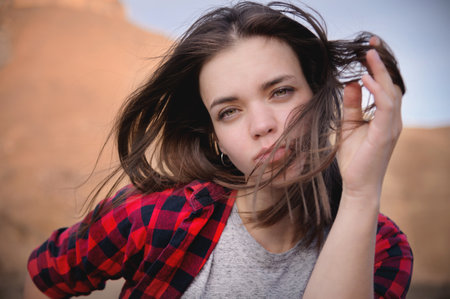 Portrait of an attractive Caucasian young woman in a checkered red shirt against a background of mountains. Bliss and pleasure in the mountains. The wind blows your hairの写真素材