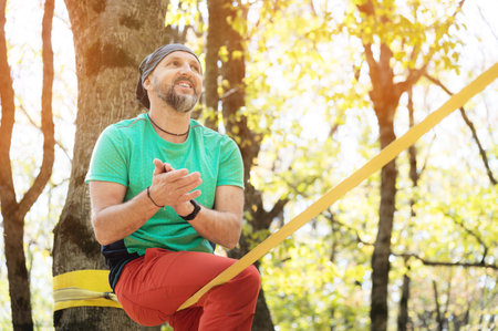 Portrait of a bearded man in age stands near a taut slackline in an autumn forestの写真素材
