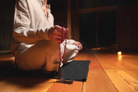 Close up of mens hands with rosary. Young man doing yoga indoors on a black rug. spirituality and practice religion conceptの写真素材
